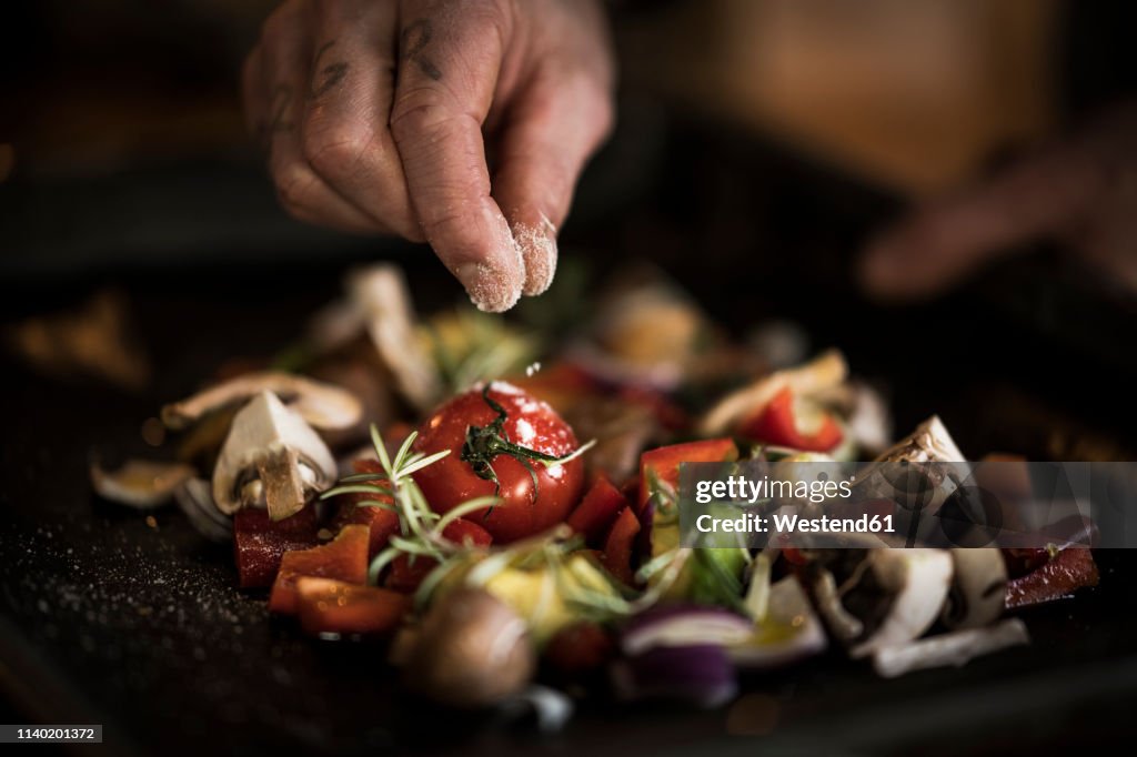 Hand seasoning vegetables ona a baking tray