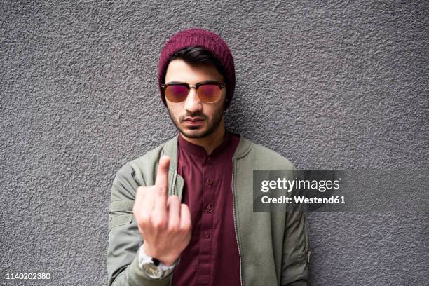 portrait of offensive man in mirrored sunglasses and purple hat showing fuck at camera. isolate on concrete textured background - doigt dhonneur stockfoto's en -beelden