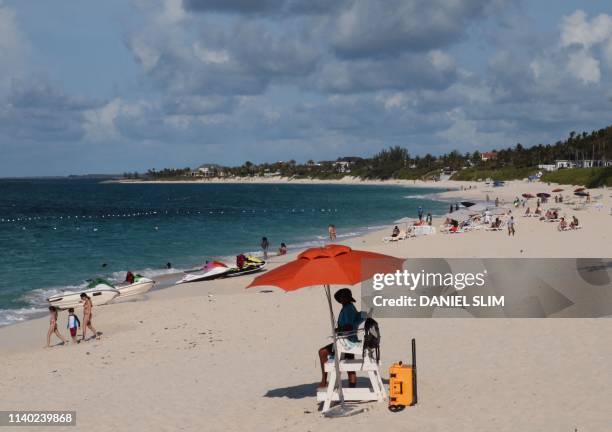 Lifeguard sits under the umbrella while watching people enjoy Paradise island beach, Nassau, Bahamas on April 29, 2019.