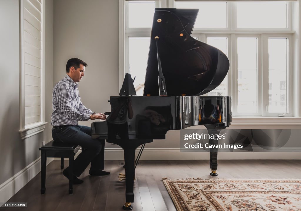 Man playing baby grand piano in a bright room