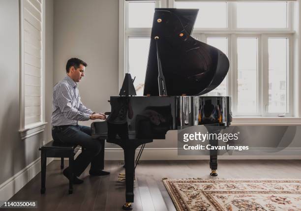 man playing baby grand piano in a bright room - playing piano stock pictures, royalty-free photos & images