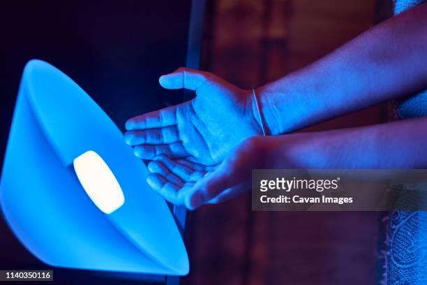 close up view of hands illuminated by a blue light bulb led light - luminothérapie photos et images de collection
