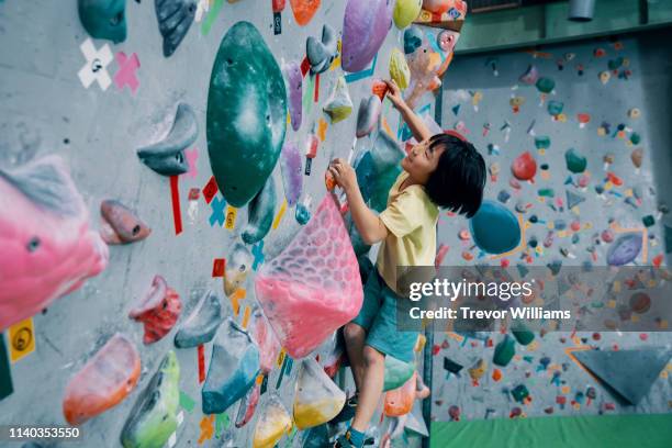 one young girl climbing a bouldering wall at a rock climbing gym - kinder klettern stock-fotos und bilder