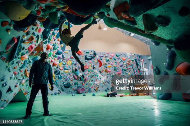 one young girl climbing with the support of her coach at a rock climbing gym - extreme sports kids stock pictures, royalty-free photos & images