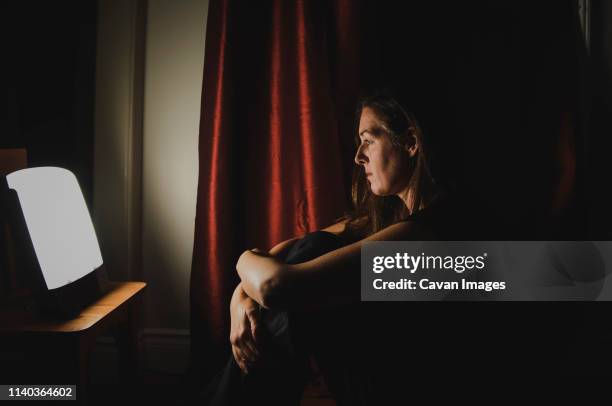 profile of woman sitting looking at light therapy lamp in a dark room - sad dark room stock pictures, royalty-free photos & images