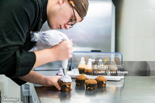 young pastry chef is putting butter cream on cupcakes with sac a poche - pastry chef stock pictures, royalty-free photos & images