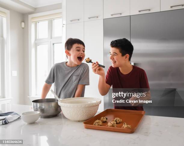 older boy feeding cookie dough to young boy in modern kitchen - eating cookies foto e immagini stock