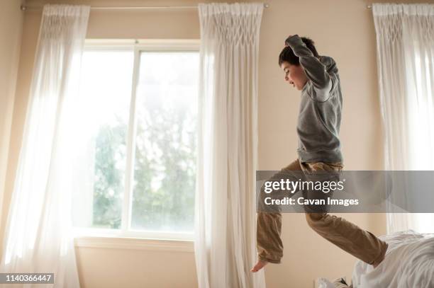 young boy leaps of bed in bedroom with joyful expression - boys jumping stock pictures, royalty-free photos & images