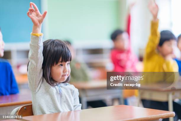 niedliche grundschule mädchen heben hand im klassenzimmer - cute japanese boy stock-fotos und bilder