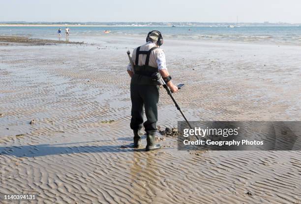 Male detectorist using metal detector at low tide, sandy beach Studland Bay, Swanage, Dorset, England, UK.