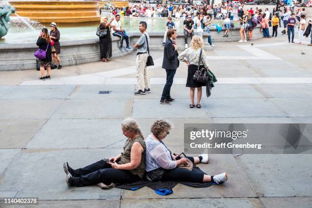 London, Trafalgar Square, tourists leaning back to back on smart phones.