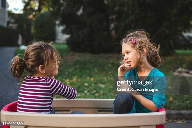 two little girls sit together having a conversation inside a wagon - family with two children foto e immagini stock