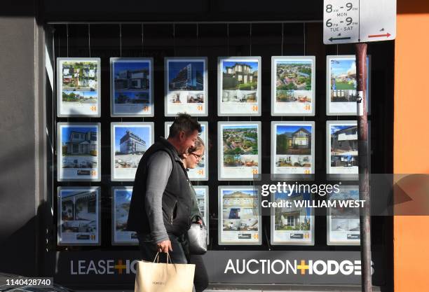Couple walks past a real estate agent's window advertising houses for sale and auction in Melbourne on May 1, 2019. - Australian property prices fell...