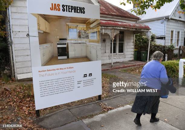 Woman walks past a real estate agent's sign advertising a house for auction in Melbourne on May 1, 2019. - Australian property prices fell faster in...
