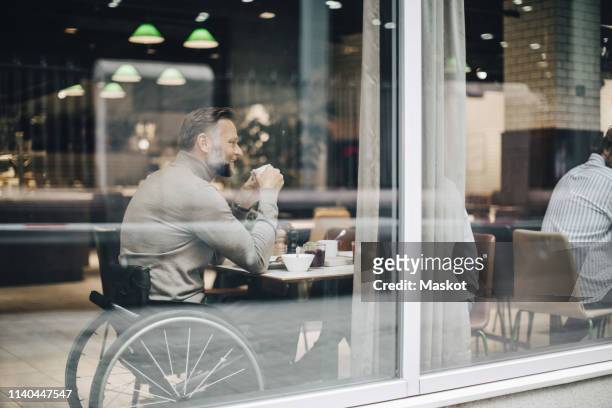 Businessman having breakfast with businesswoman at table in restaurant seen through window glass
