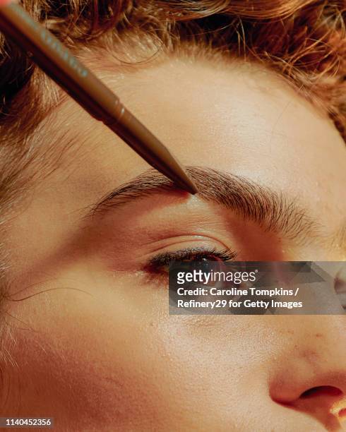 closeup of a young confident woman filling in her eyebrows - eyebrow pencil stockfoto's en -beelden