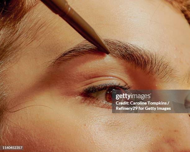 closeup of a young confident woman filling in her eyebrows - eyebrow pencil stockfoto's en -beelden