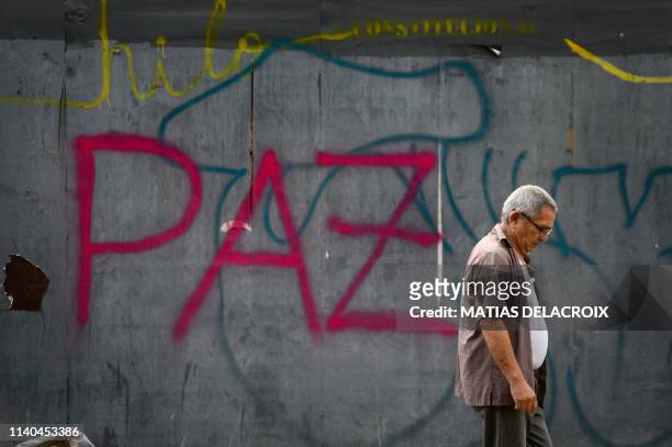 Man walks in front of a graffiti reading "peace" in Caracas on May 1, 2019 after a day of violent clashes on the streets of the capital spurred by...