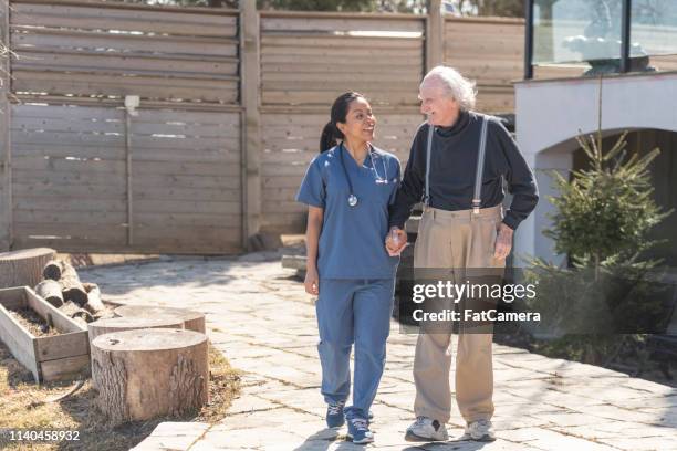 pflegeberuferin geht mit älteren mann auf pflegeheim-campus nach draußen - medicaid stock-fotos und bilder