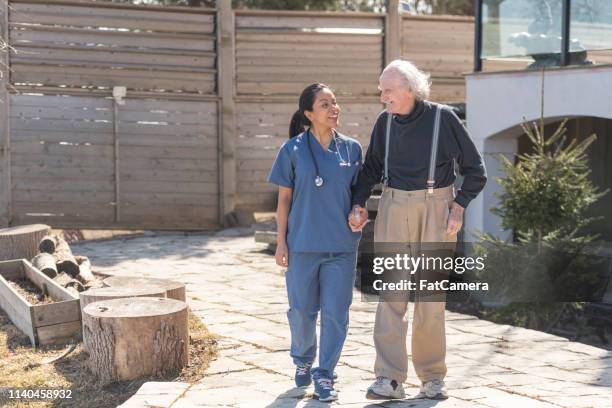 healthcare professional walks outdoors with elderly man on nursing home campus. - medicaid stock pictures, royalty-free photos & images