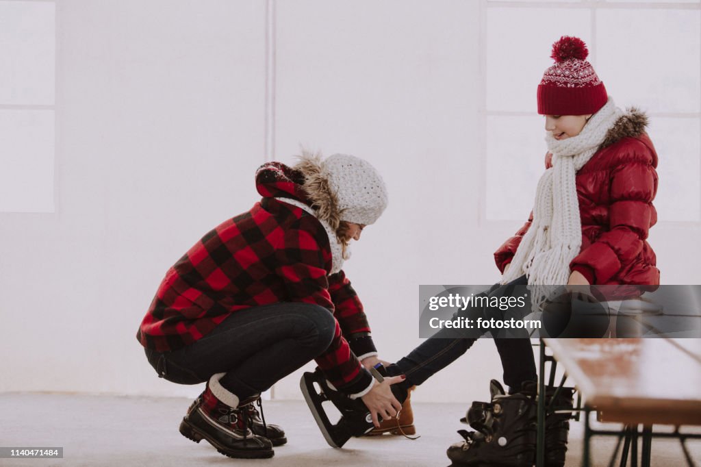 Mother putting ice skates on daughter's feet