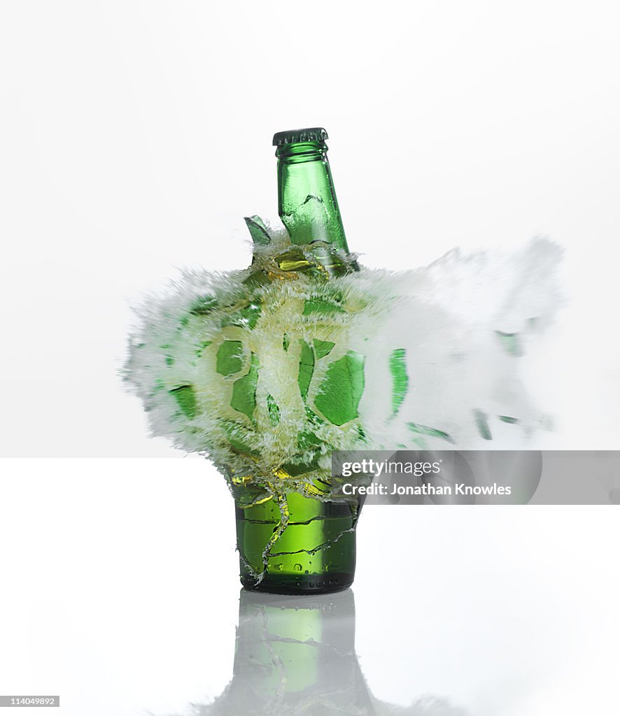 A beer bottle exploding on  a white background