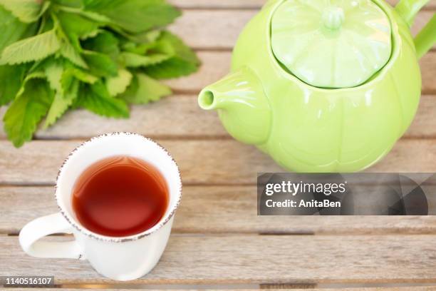 melissa officinalis cup of tee and kettle on wooden background - lemon balm stockfoto's en -beelden