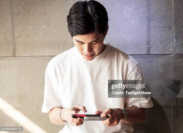 jeune homme asiatique restant jouant un jeu sur le téléphone avec le bonheur - regarder vers le bas photos et images de collection