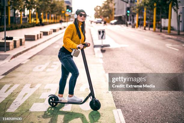 eine urbane frau, die musik über die kopfhörer hört, um den verkehr in der innenstadt der stadt zu verbinden - elektro tretroller stock-fotos und bilder