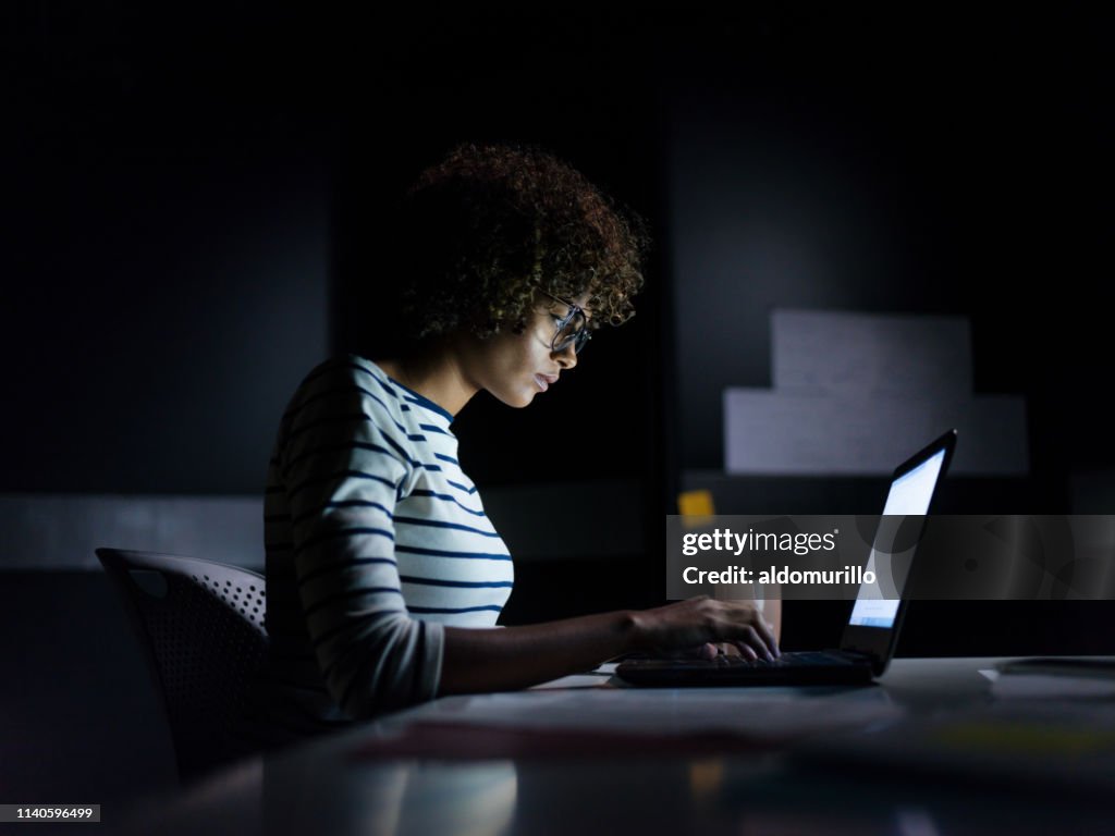 Konzentrierte Geschäftsfrau, die spät mit ihrem Laptop arbeitet