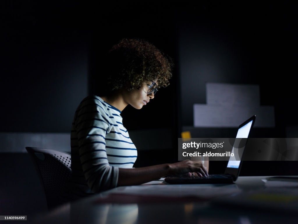 Mujer de negocios concentrada trabajando hasta tarde con su Laptop