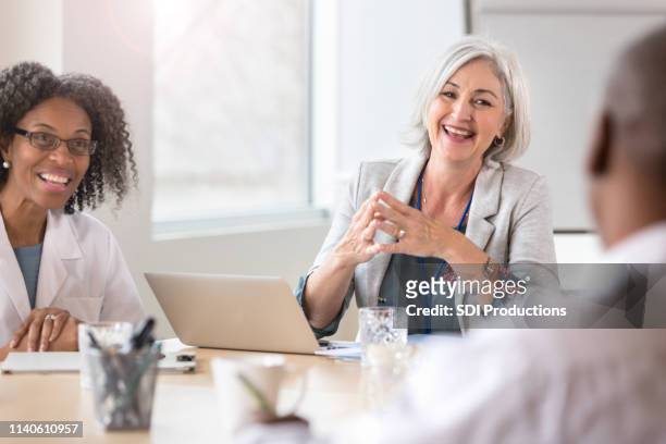 smiling hospital executive facilitates meeting - medical leadership stock pictures, royalty-free photos & images