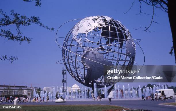 Wide shot of people walking on a pavement near the Unisphere, on a sunny day, New York World's Fair, Flushing Meadows Park, Queens, New York, June...