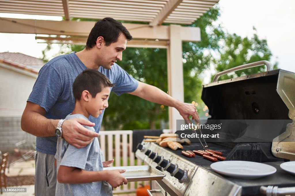 Father teaching son how to grill hot dogs and bonding