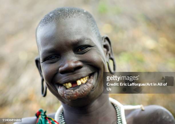 Portrait of a surma tribe woman with enlarged lip and ears and toothy smile, Tulgit, Omo valley, Ethiopia on October 25, 2008 in Tulgit, Ethiopia.