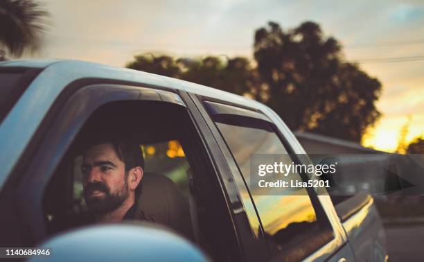 el hombre barbudo en un camión va a conducir al atardecer - conductor oficio fotografías e imágenes de stock