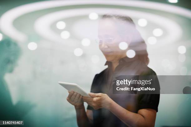 senior woman standing with smart tablet computer - halo symbol stock pictures, royalty-free photos & images