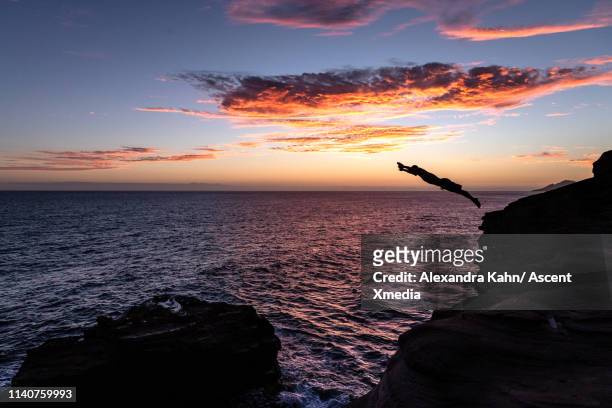 diver launches from cliff into ocean at sunset - leap of faith activity stock pictures, royalty-free photos & images