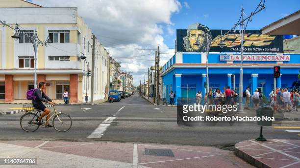 El Prado' promenade. A man rides in bicycle while a group of tourists look at a 'Che Guevara' sign on top of a store.