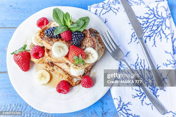 gluten free french toast with banana, raspberries, strawberries, blackberries and maple syrup on blue rustic wood background - continental breakfast stock pictures, royalty-free photos & images
