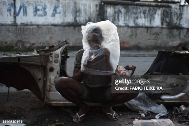 Crack smokes crack beside the shell of a disused and burnt out car in the Sem Terra favela in Complexo da Mare, Rio de Janeiro, on April 29, 2019.