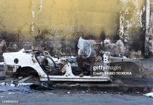 Crack smokes crack beside the shell of a disused and burnt out car in the Sem Terra favela in Complexo da Mare, Rio de Janeiro, on April 29, 2019.