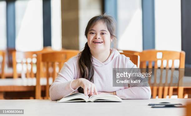 teenage-mädchen mit down-syndrom-lesung in bibliothek - lernbehinderung stock-fotos und bilder