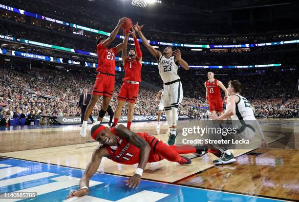 Tariq Owens of the Texas Tech Red Raiders falls on the court as Xavier Tillman of the Michigan State Spartans battles for the ball with Jarrett...