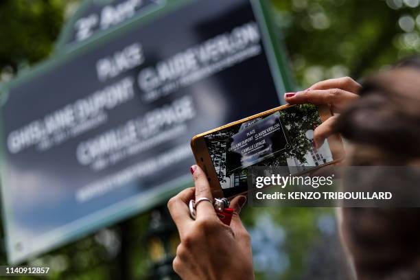 This picture taken on May 3, 2019 in Paris shows a woman taking a picture of a street sign in tribute to Ghislaine Dupont and Claude Verlon, two...