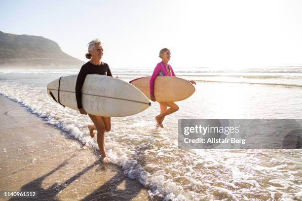 senior women going for a morning surf in the sea - active seniors stock pictures, royalty-free photos & images