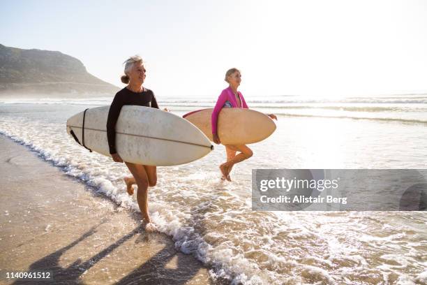 senior women going for a morning surf in the sea - jovem de espírito - fotografias e filmes do acervo