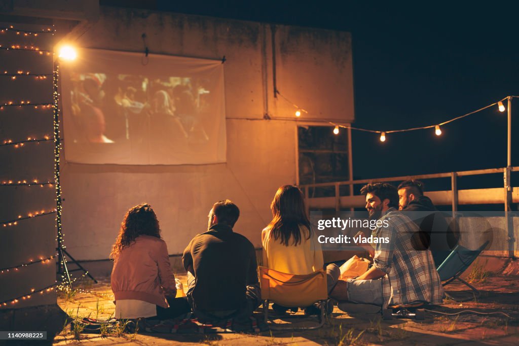 Friends watching a movie on a building rooftop terrace
