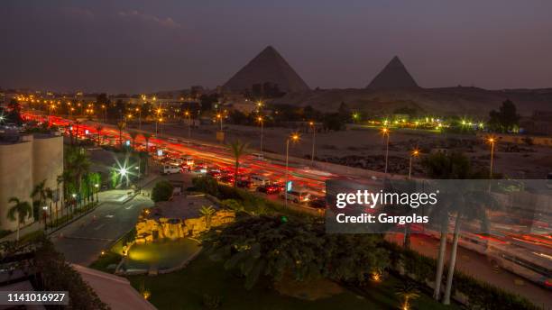 el tráfico del cairo y ver las pirámides por la noche - pirámide estructura de edificio fotografías e imágenes de stock