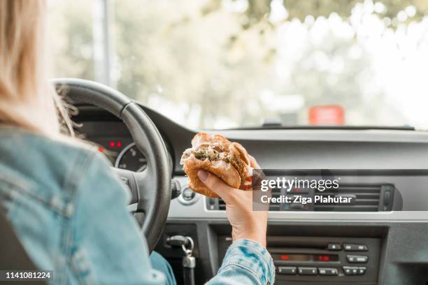 holding a bitten burger while drivinga car - burger car stock pictures, royalty-free photos & images